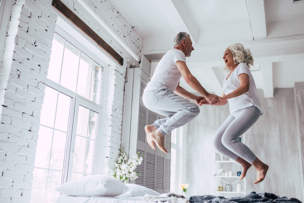Older-healthy-couple-jumping-on-bed