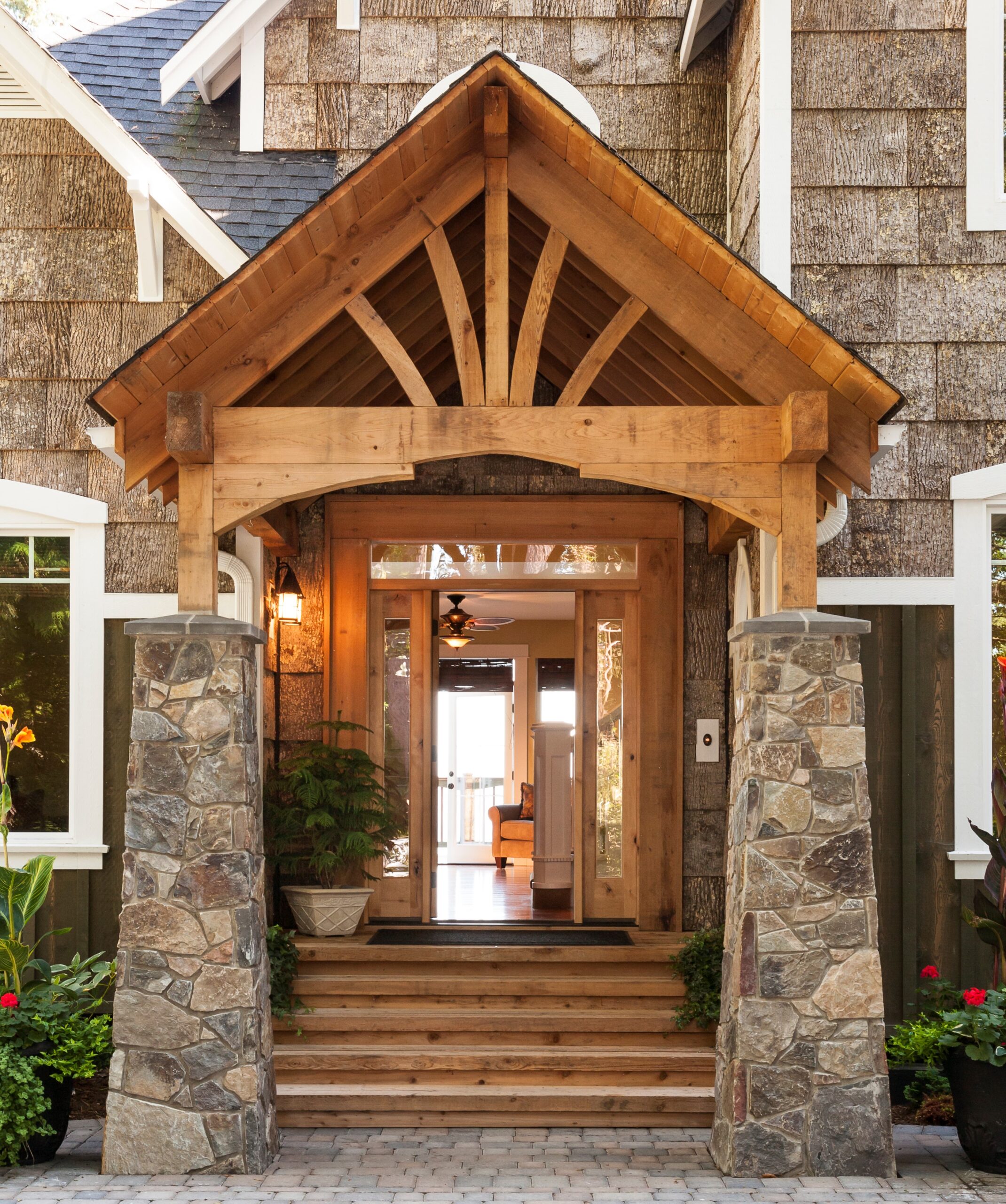 Stone and wood front porch entryway to upscale country house with open front door and paving stone driveway.