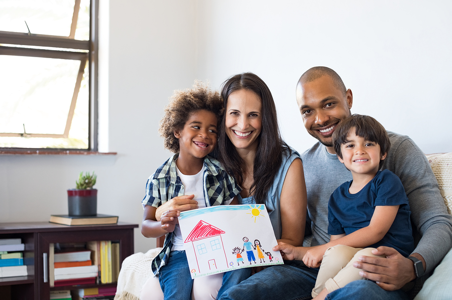 Proud parents showing family painting of son sitting on sofa at